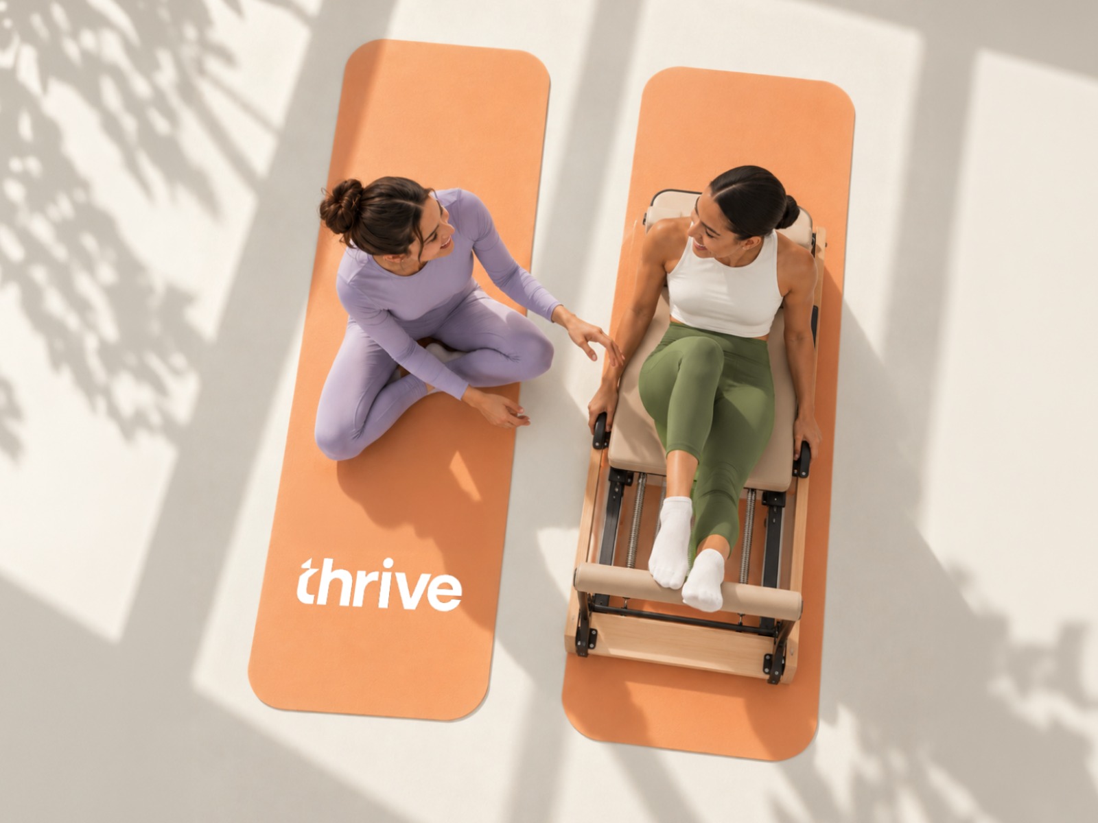 Two women on orange Thrive mats in a pilates studio
