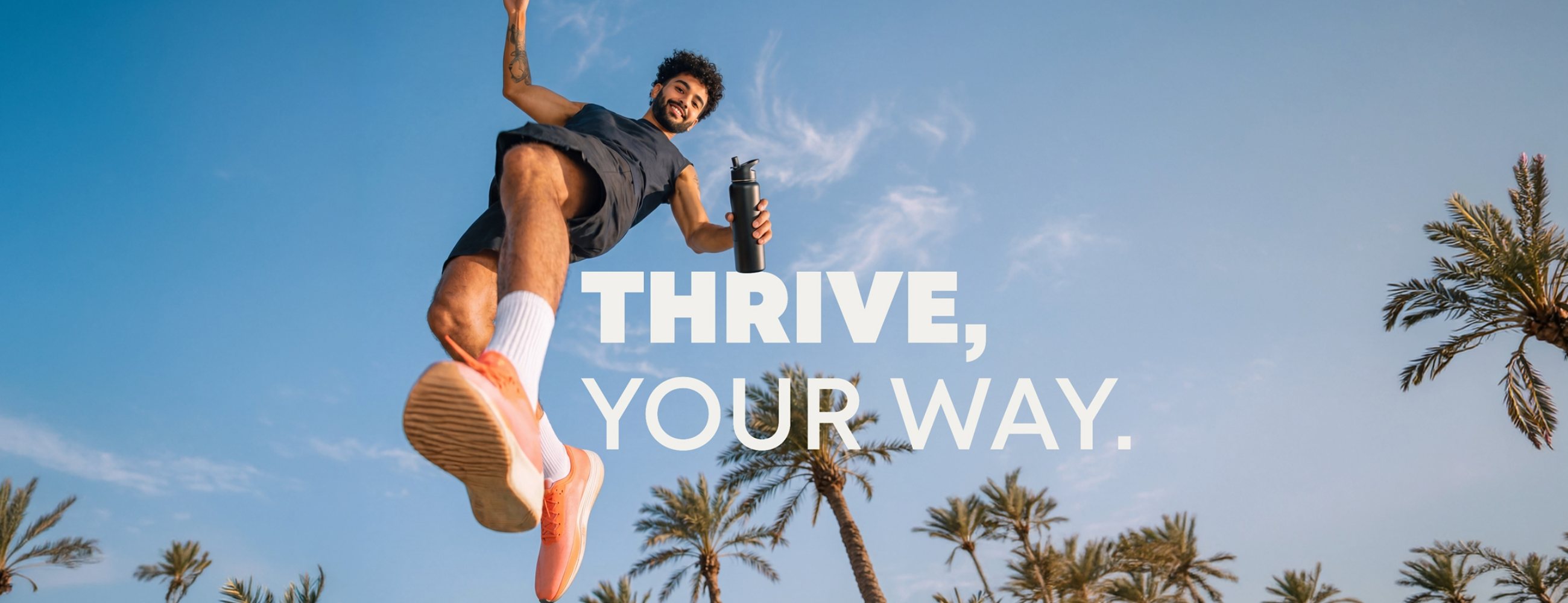 Man jumping mid-air under a blue sky with palm trees, holding a water bottle. Text: Thrive, your way.